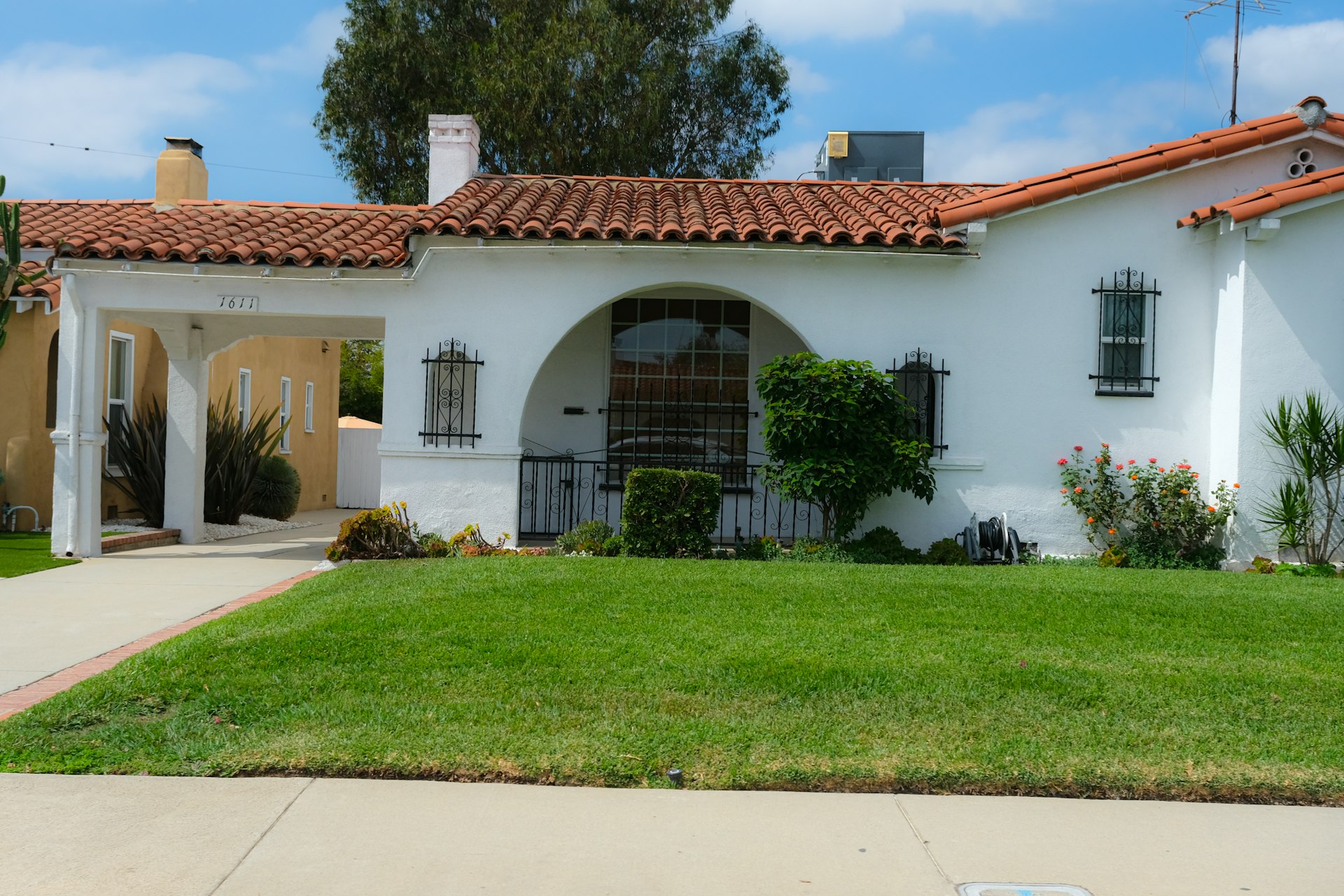 White stucco house with a red tile roof and green lawn under a blue sky